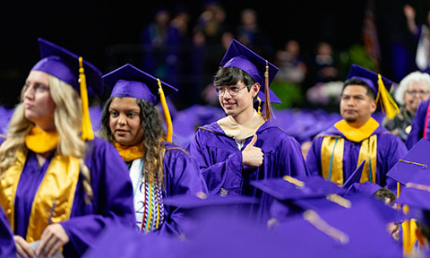 Graduates in purple caps and gowns, one giving a thumbs up.