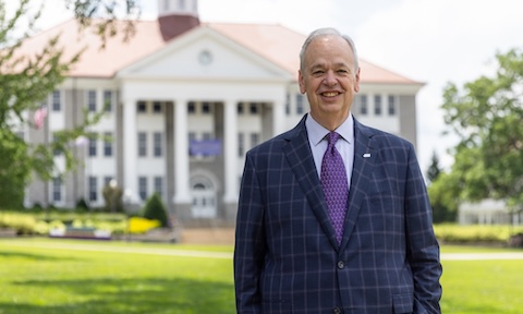 Jim Schmidt smiling at camera in front of Wilson Hall on the Quad at JMU.