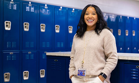 Female student teacher standing in front of blue school lockers
