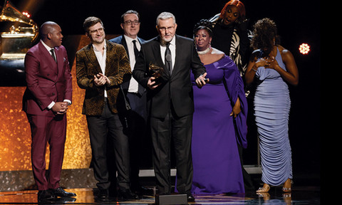 Grammy winners standing on stage in formal attire