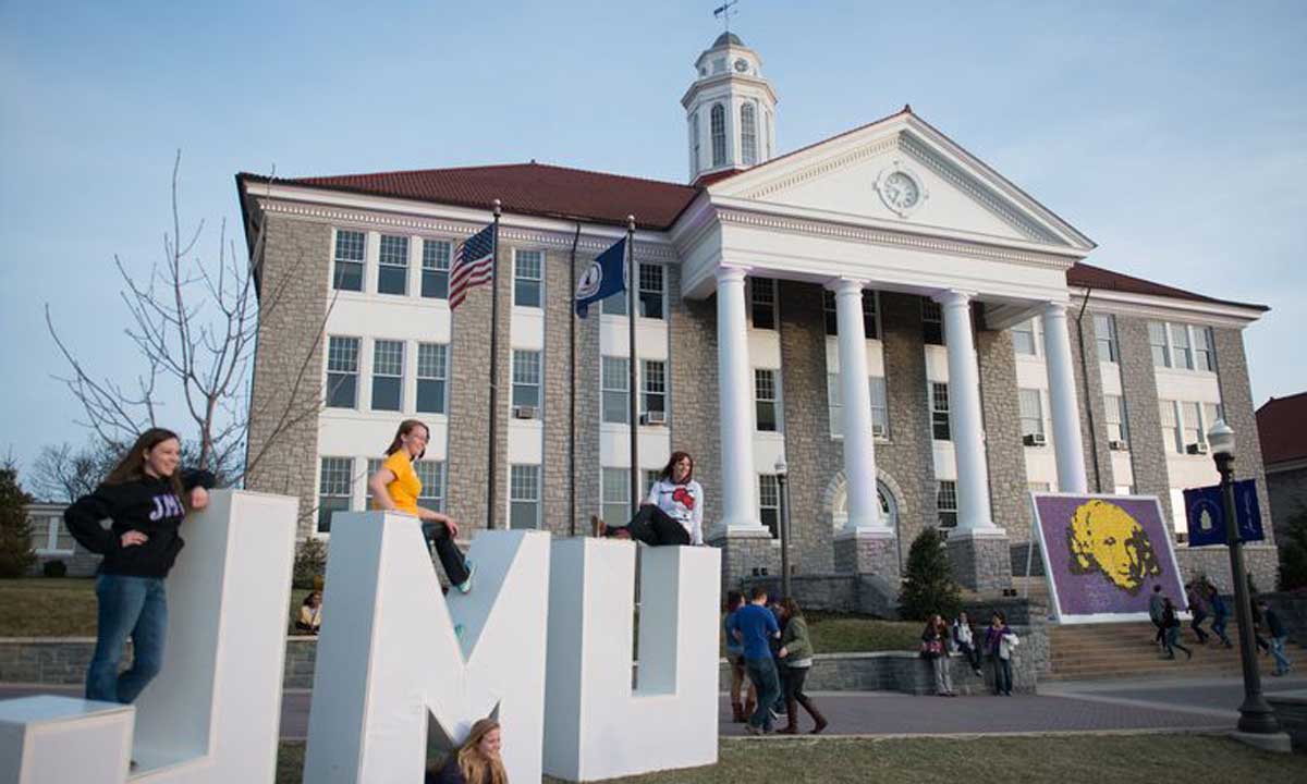 Students lined up to pose with the J-M-U letters set up on the Quad for MadisonFest. James Madison's likeness made from 3000 cupcakes in the background.