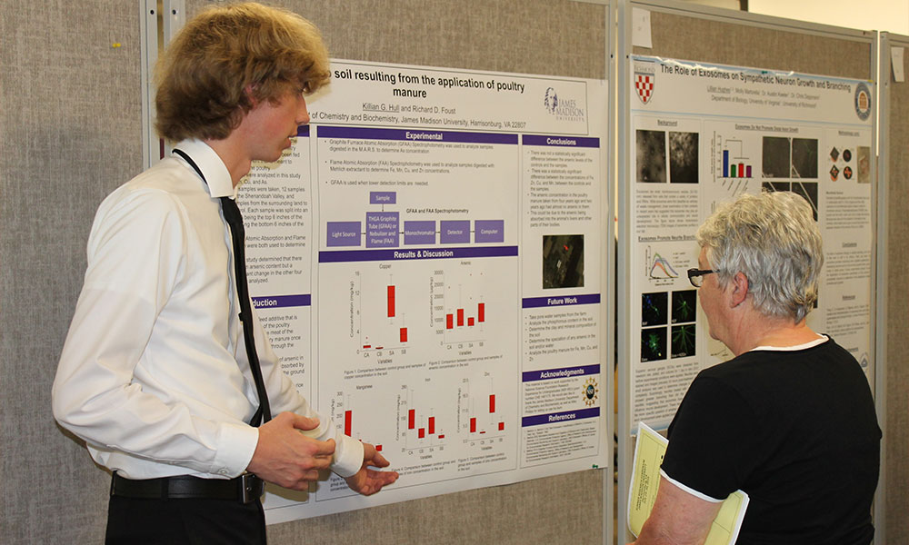 Student points to his poster as a faculty member standing near him listens to his presentation