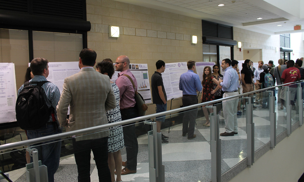 photo of several groups of people discussing several posters in a hallway.