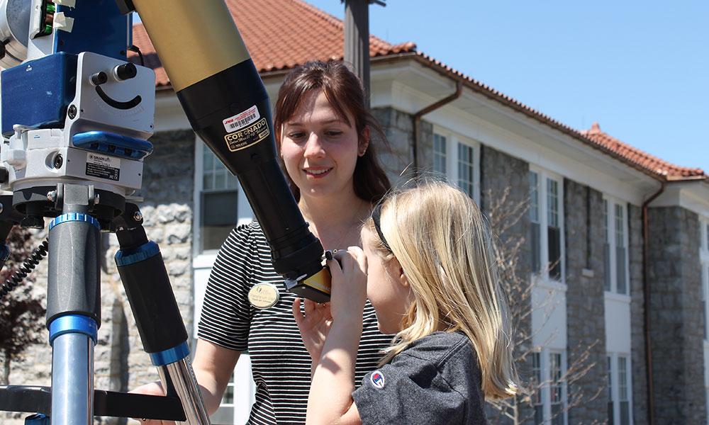 Calah Mortensen helps a visitor look at the sun through a solar telescope set up near the John C. Wells Planetarium.