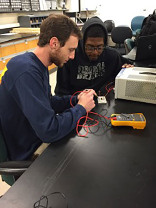 Alex and Javal sitting at a work bench and building a sensor in the lab.