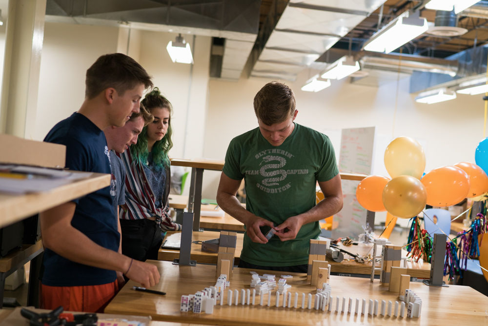 Students smiling, lining up dominoes. 