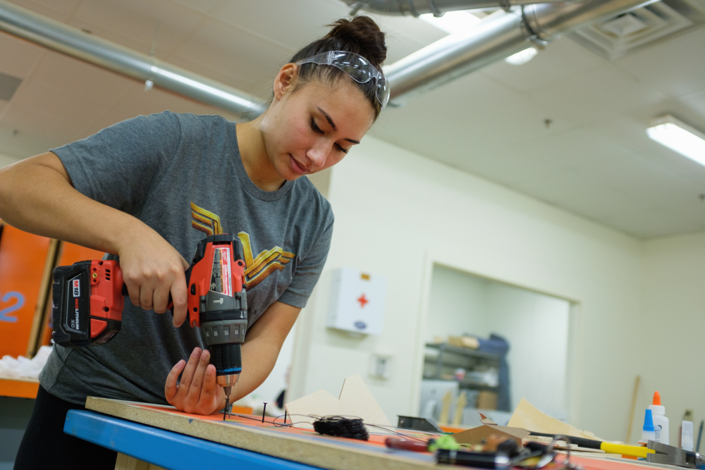 a student concentrating on using a drill in a wood shop class