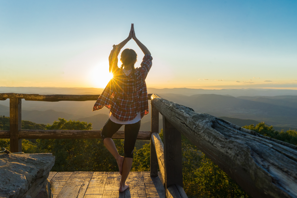 Girl doing a yoga pose at sunset on high knob tower overlooking a beautiful view of the mountains. 