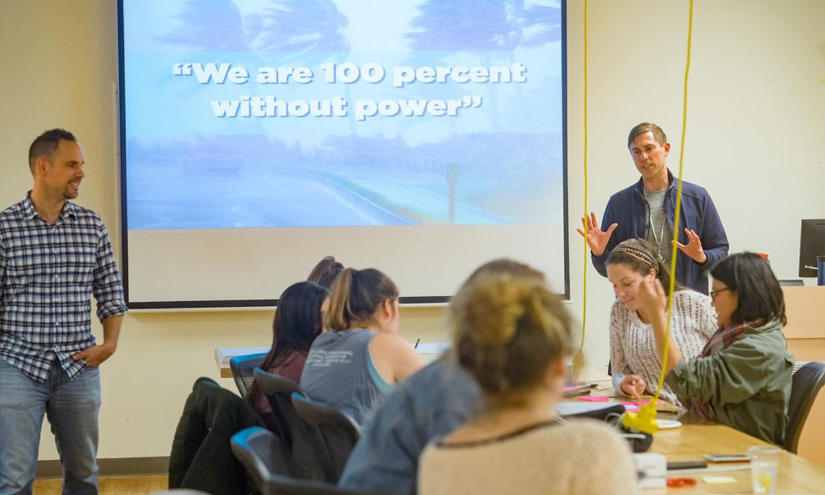 Wide angle of a classroom with a powerpoint visible in the background with the words 