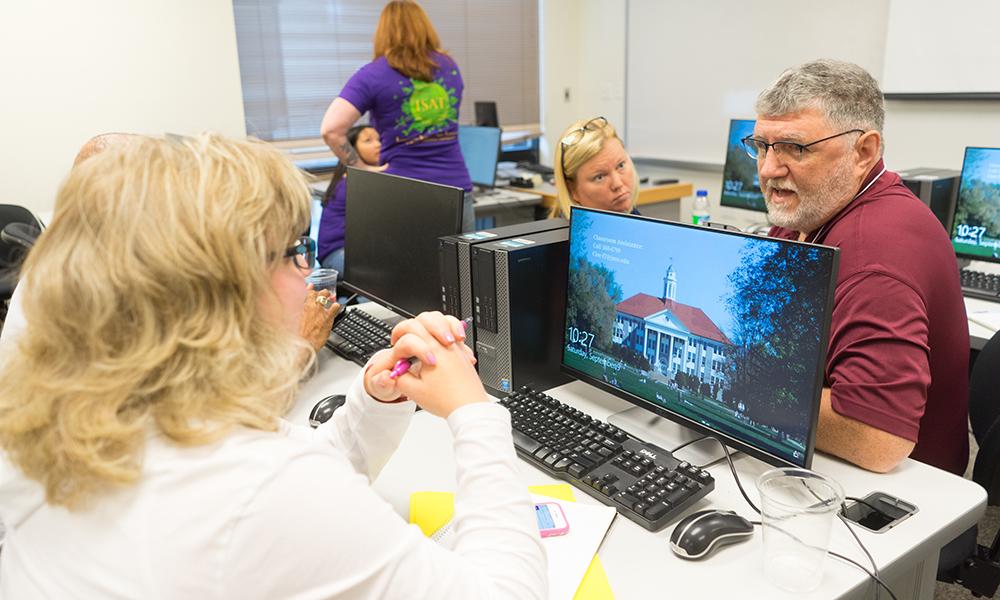 Photo of teachers at computers in classroom talking to each other