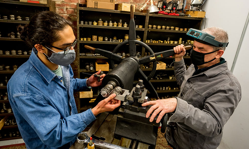 Engineering student repairing a jewelry machine with the owner.