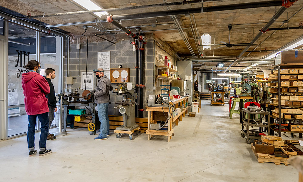 Engineering students standing in a jewelry machine shop with owner.