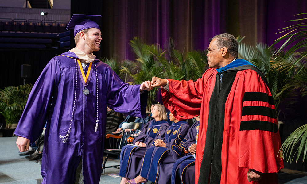 Graduate bumping fists with professor