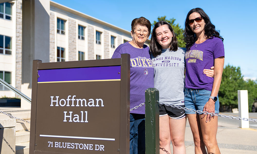 Three generations of college women stand outside a residence hall.