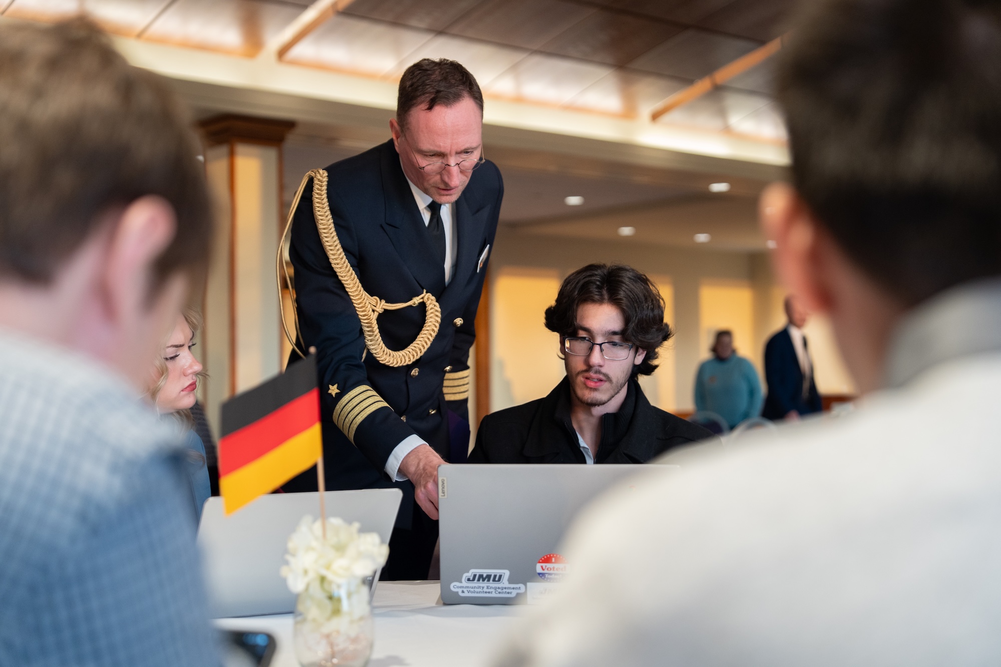 A formal event featuring an officer in military attire assisting students at laptops.