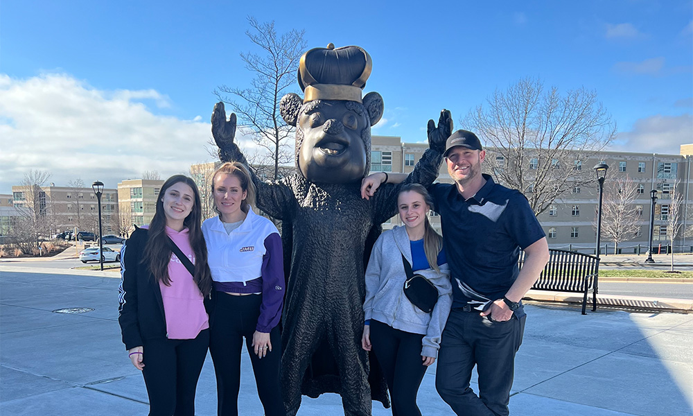 A family poses next to a large Duke Dog statue wearing a crown on a sunny day.
