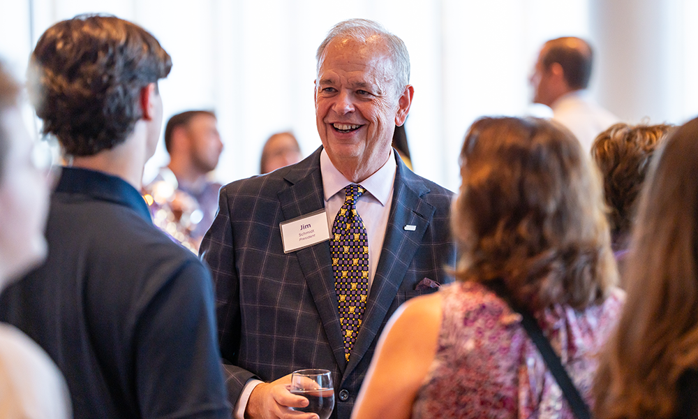 President Jim with a cheerful expression engages in conversation at a social event.