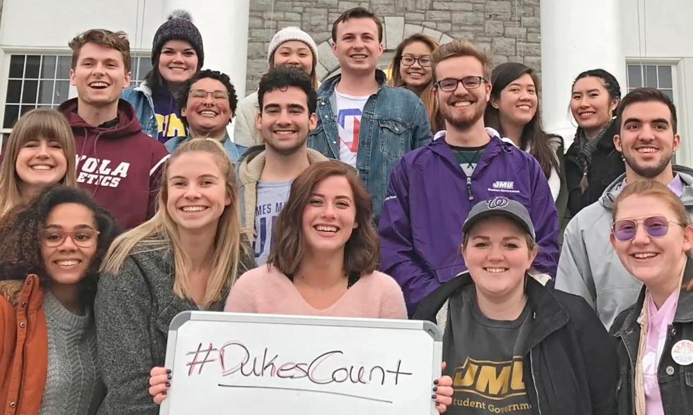 Seventeen students stand in front of Wilson Hall with #DukesCount board.