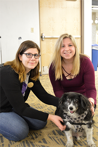 2 women pose with a dog as they pet it