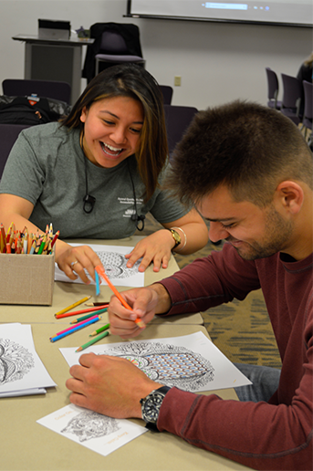 2 people sit at a table coloring blank outlines with colored pencils