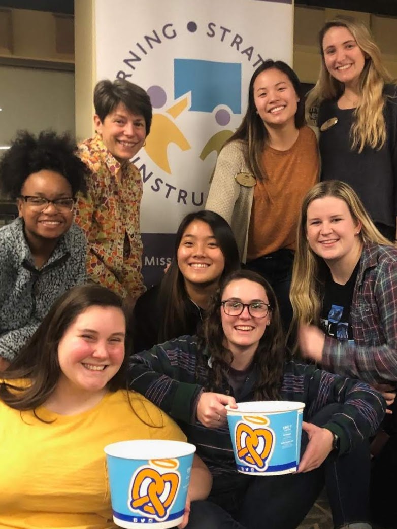 team smiling in front of L-S-I banner, two holding pretzel buckets