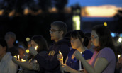 Students hold candles as the sun sets behind them