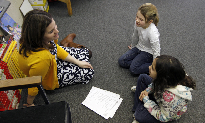 Two children sit on the floor with their teacher