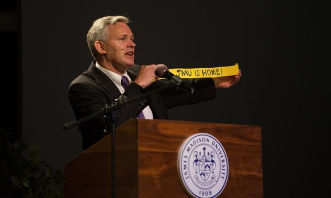 President Alger holds streamer that says JMU is Home