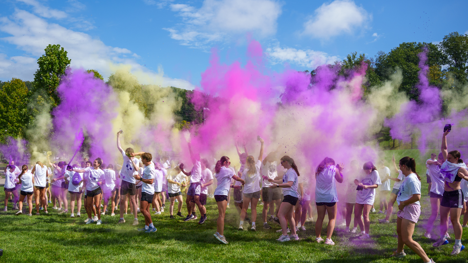 students throwing purple and yellow powder in the sky