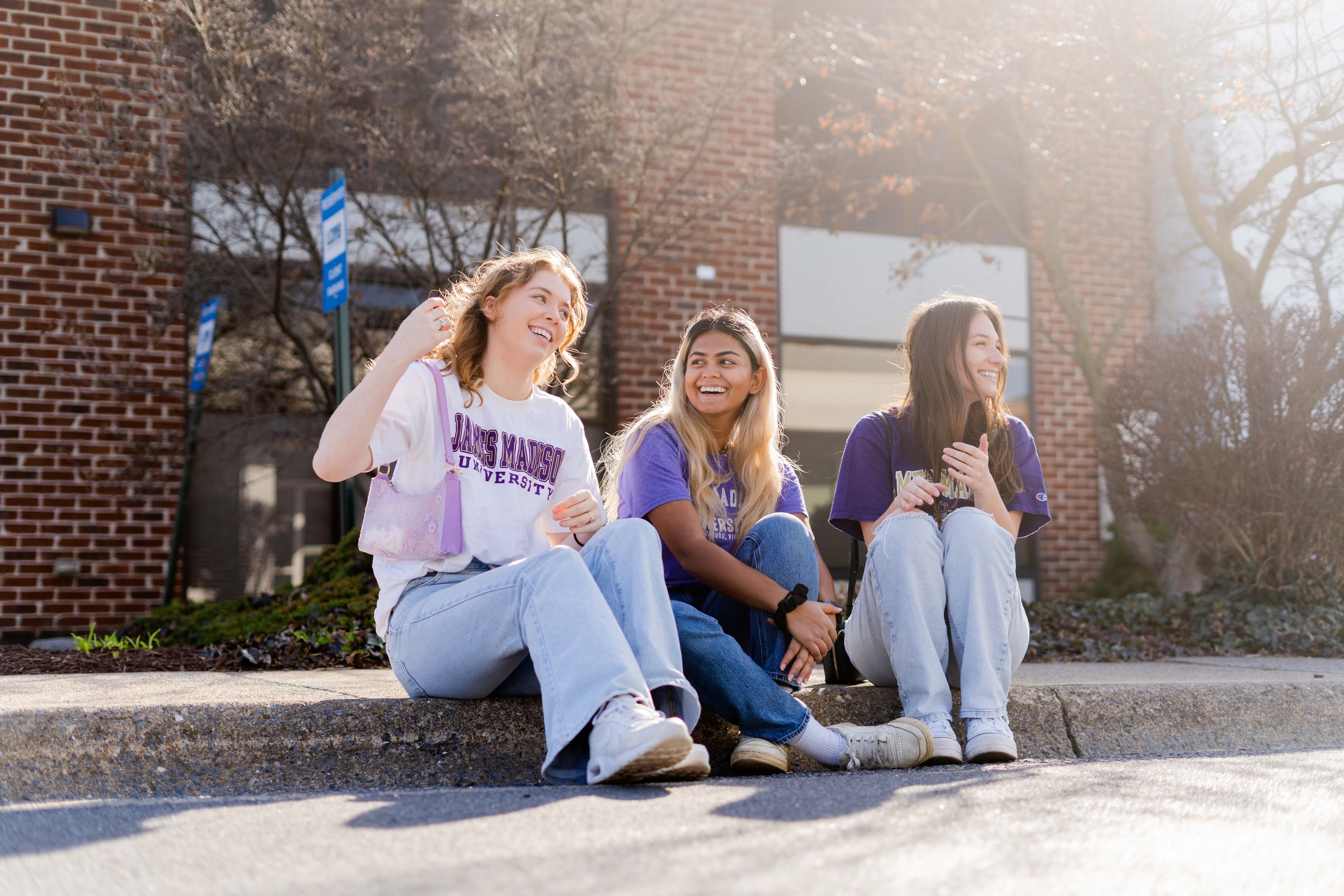 Three college students sitting on a curb in a downtown area