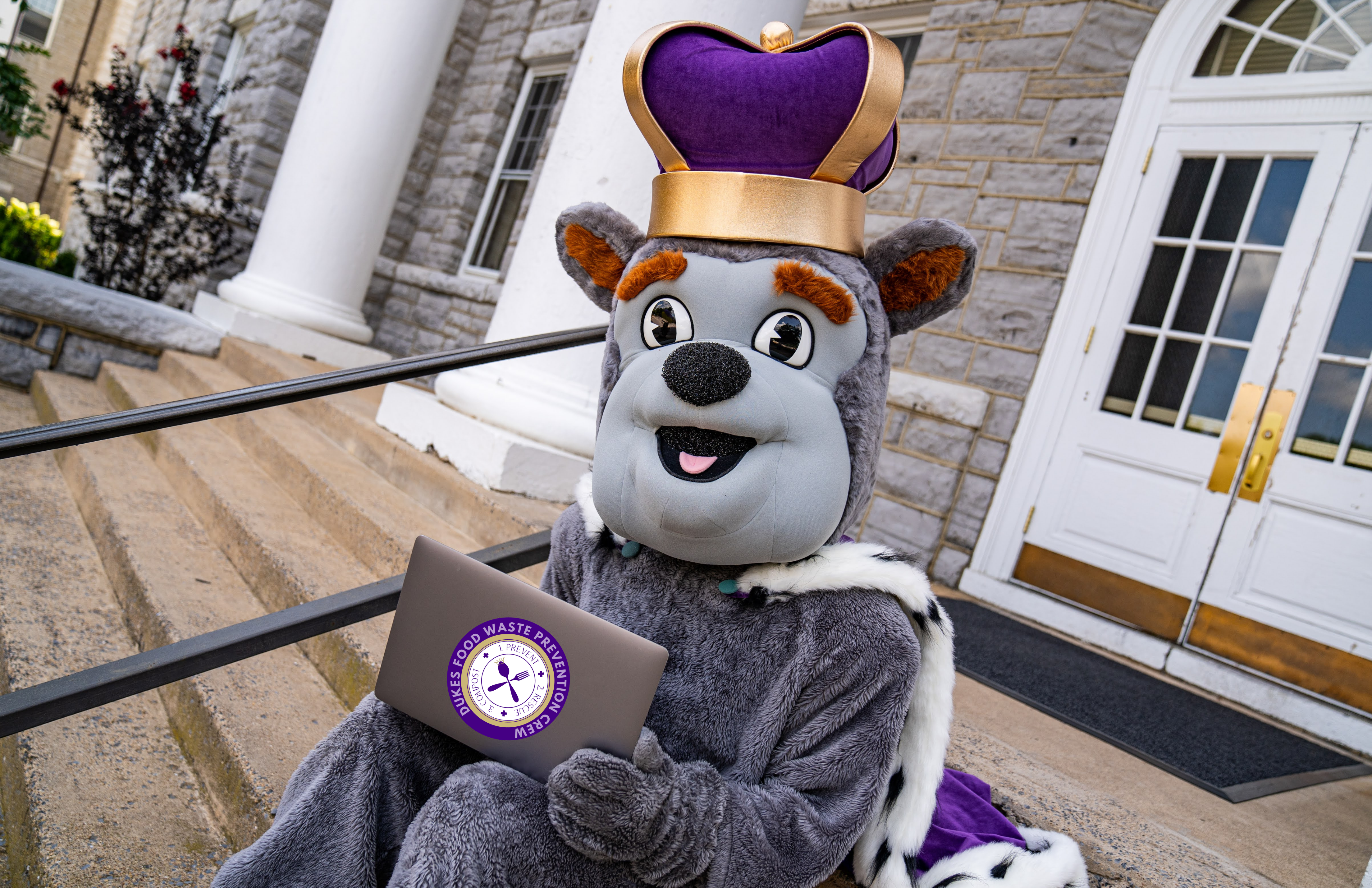 School mascot holding laptop with food waste prevention program sticker
