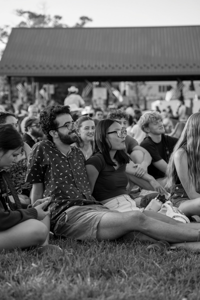 A crowd of people sit together outside in the summer