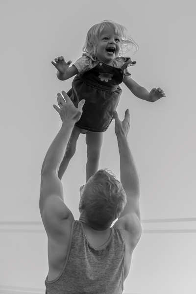A toddler laughs as their parent throws them up in the air