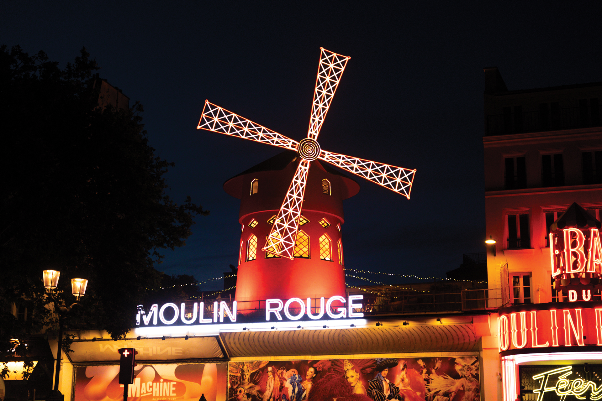 Neon-lit windmill atop the Moulin Rouge at night, with the glowing "MOULIN ROUGE" sign below.