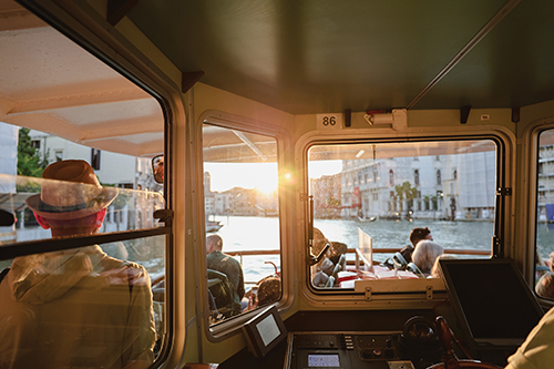 Passengers seated inside a boat cabin at sunset, looking out through large windows toward a marina.