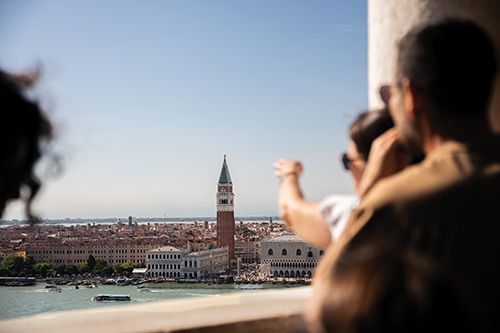 People on a terrace overlooking Venice, with St. Mark’s Campanile and the lagoon in the distance.