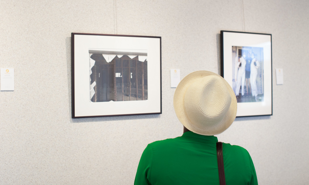 An individual's back as they look at some framed photography on a light colored wall.