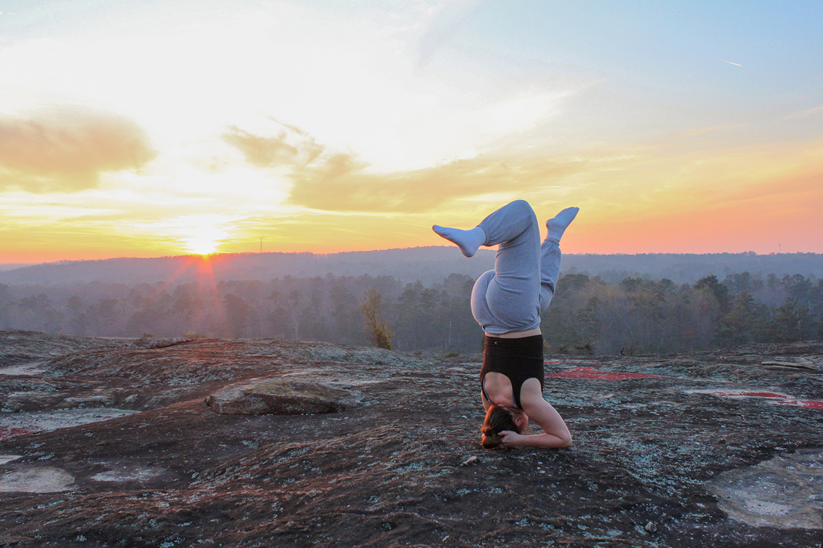 A person practicing a headstand on a rocky surface during a beautiful sunset.