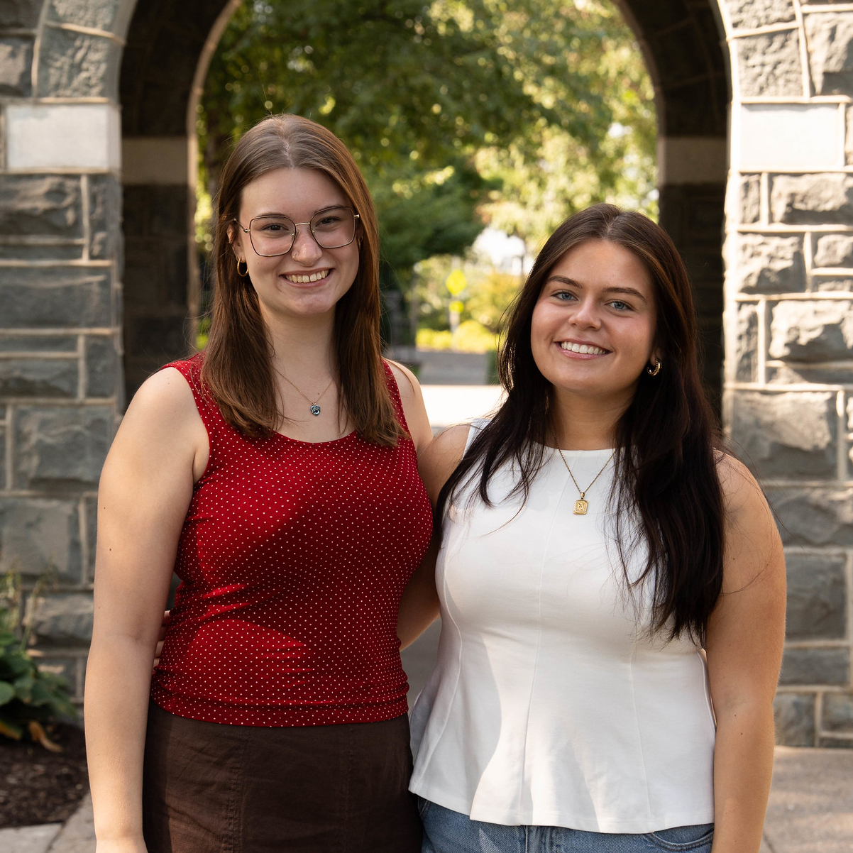 Two smiling student employees stand side by side in an outdoor setting