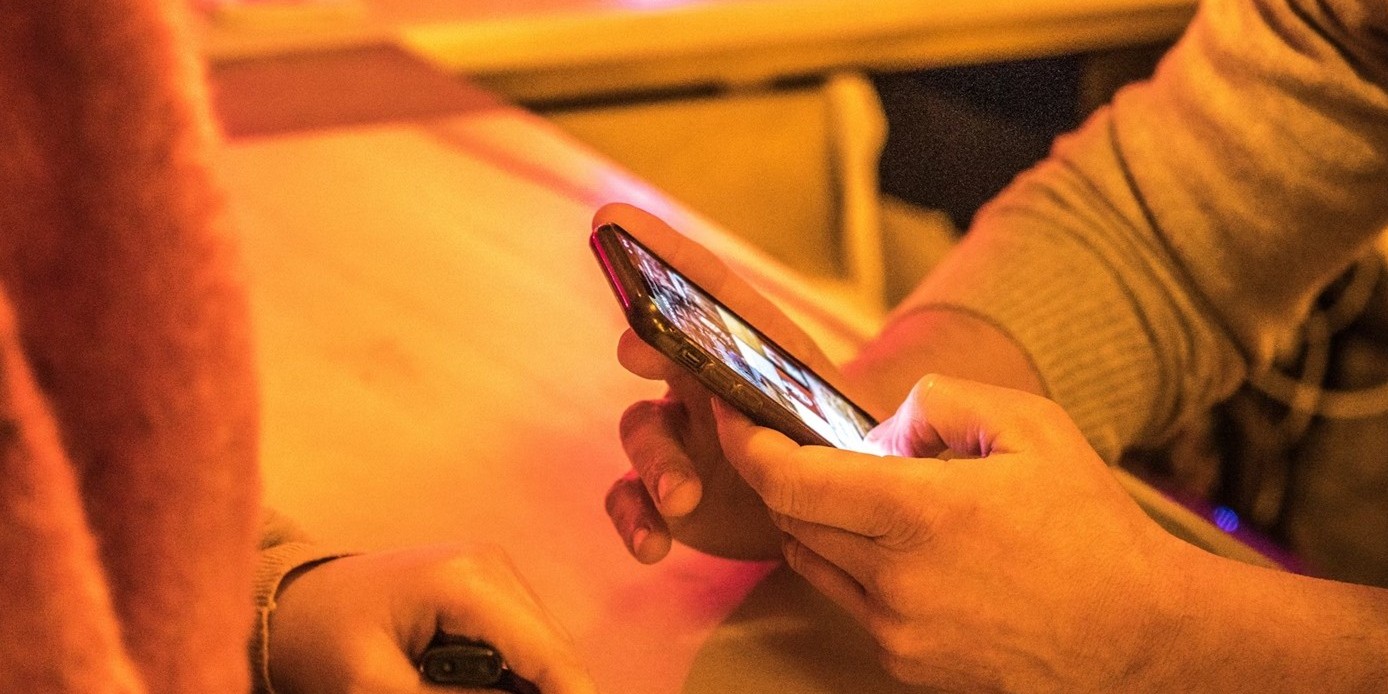 Person looking at their phone with someone sitting across the table from them.