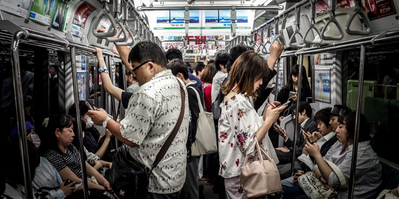 Public metro or bus that is crowded with many folks both standing or sitting on the side benches.