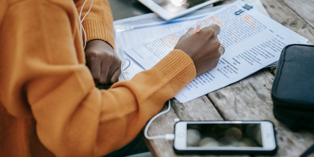 Person studying while listening to music on headphones through their phone.