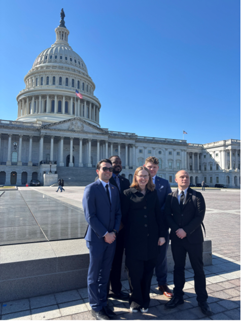 Group of individuals posing in front of the U.S. Capitol building on a clear day.