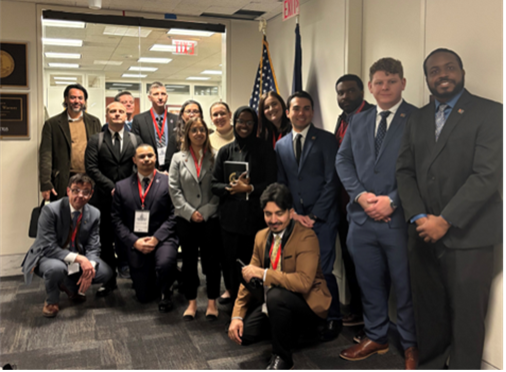 Group photo of a diverse team of professionals and students at a formal event, standing in front of an American flag.