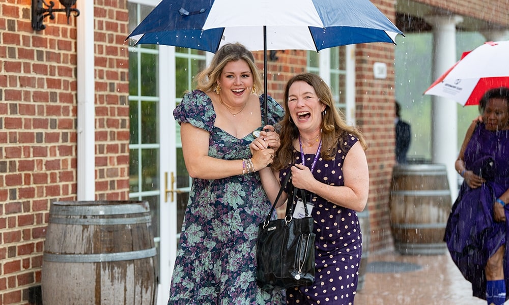 Two women joyfully share an umbrella while laughing in the rain, showcasing a moment of friendship and fun amidst a drizzly day.
