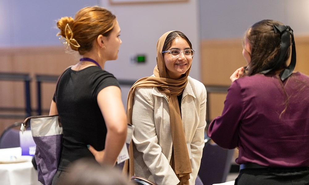 A group of three women engaged in a conversation at a networking event, showcasing diverse styles and attire.