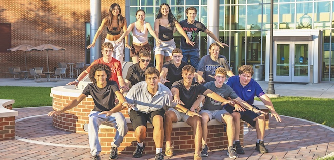 group of students sitting on firepit edge with arms spread out saying "JMU Duuuuukes"