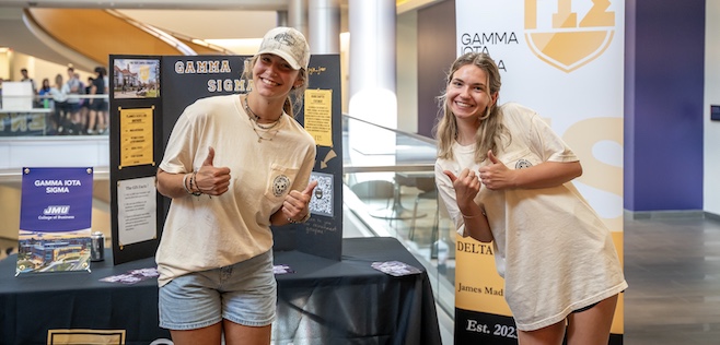 Two girls giving the thumbs-up sign in front of table at student org night