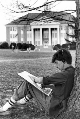 Artist sitting against a tree on the Quad wearing headphones with Wilson Hall in the background (1988)