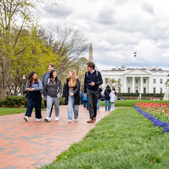 Four friends walking on a brick path near the White House, with spring flowers and the Washington Monument in the background.